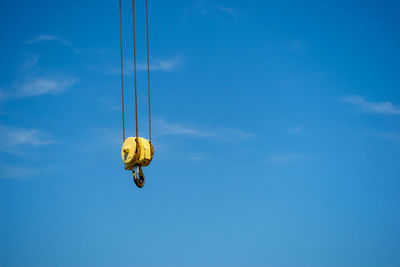 Low angle view of crane hook hanging against blue sky