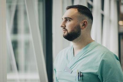 Thoughtful male nurse looking through window in hospital