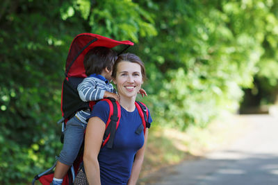 Mother with toddler child in backpack carrier is hiking in forest