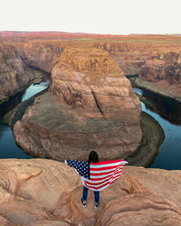 Rear view of woman holding flag while standing on rock