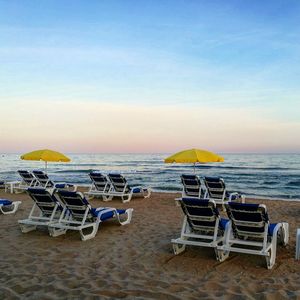 Deck chairs on beach against clear sky at sunset