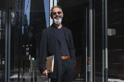 Smiling male professional with file standing by building in city