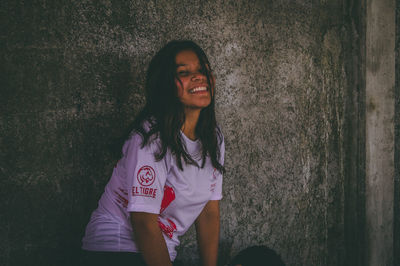 Portrait of smiling young woman standing against wall