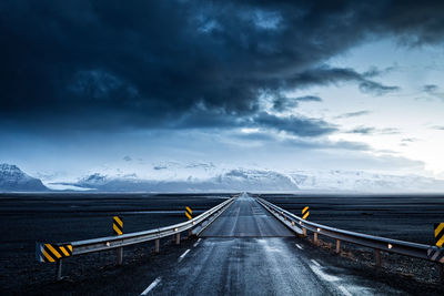 Empty road leading towards mountains against cloudy sky