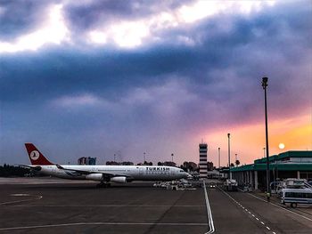 Airplane on airport runway against sky during sunset