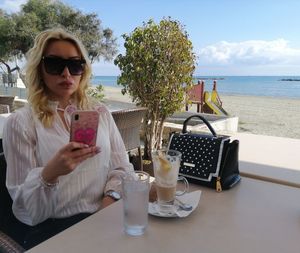 Woman wearing sunglasses using smart phone while sitting at outdoor restaurant