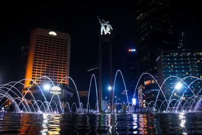 Water fountain against illuminated buildings in city at night