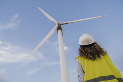 Engineer looking at rotor of tall wind turbine by blue sky