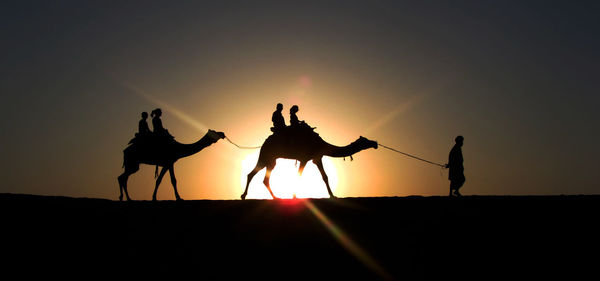 Silhouette people on desert against sky during sunset