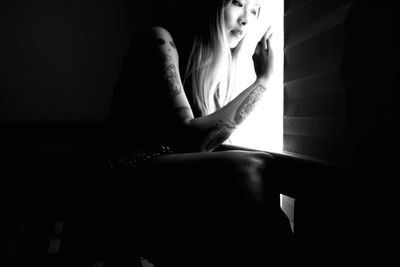 Young woman looking through window while sitting in darkroom at home