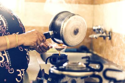 Midsection of woman straining tea in kitchen