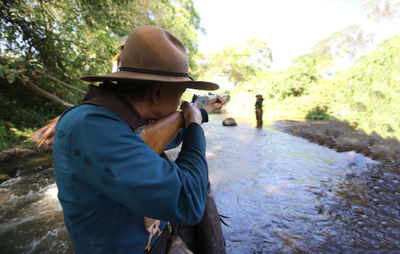 Side view of man aiming gun at male standing in river