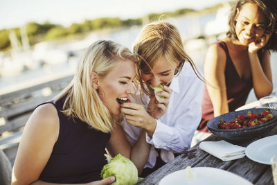 Young woman looking at cheerful blond friends sharing cabbage at picnic table