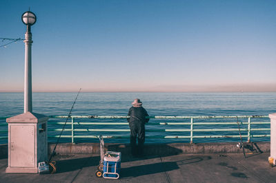 Rear view of man standing by railing against sea