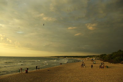 People at beach against sky during sunset