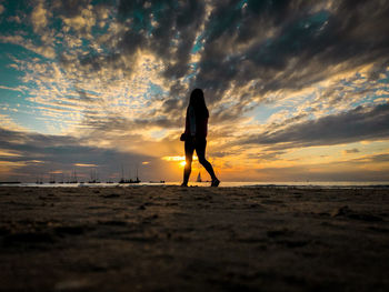 Silhouette woman walking at beach against sky during sunset