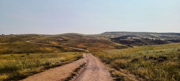 Dirt road leading towards mountains against clear sky