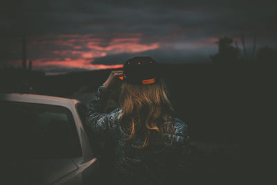 Rear view of woman wearing cap while standing by car at night