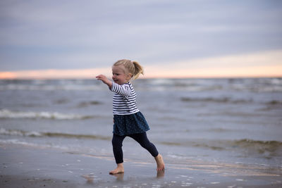 Full length of girl playing at beach against sky during sunset