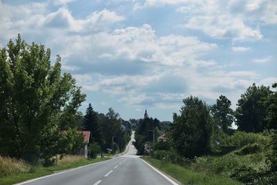 Road by trees against sky in city