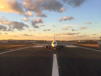 Airplane on airport runway against sky during sunset