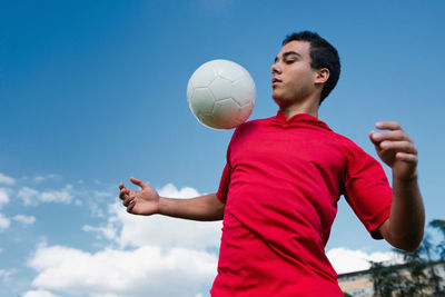 Low angle view of man playing with soccer ball against blue sky