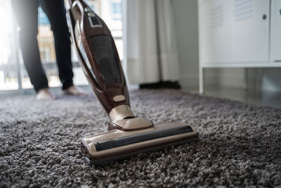 Low section of person cleaning carpet with vacuum cleaner