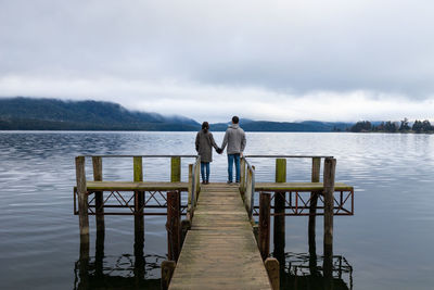 Rear view of men standing on pier over lake against sky