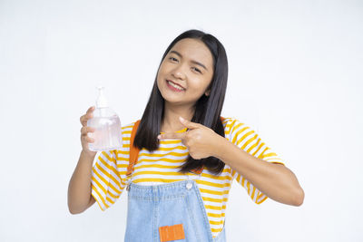 Portrait of a smiling young woman drinking glass against white background
