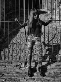 Full length of young woman standing against fence