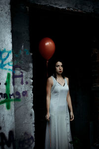 Portrait of woman holding helium balloon while standing by wall