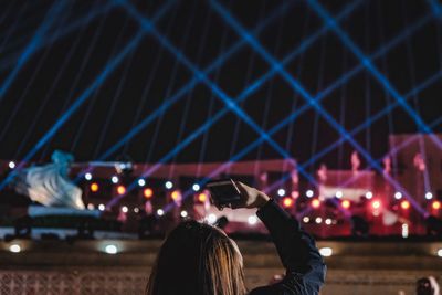 Woman photographing illuminated laser lights at night