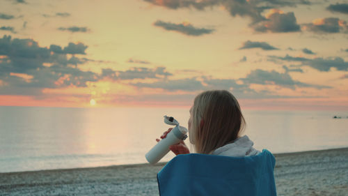 Rear view of woman photographing sea against sky during sunset