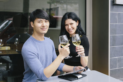 Portrait of couple toasting drinks while sitting at sidewalk cafe