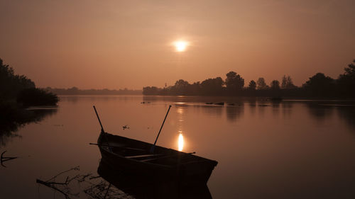 Silhouette boat moored in lake against sky during sunset