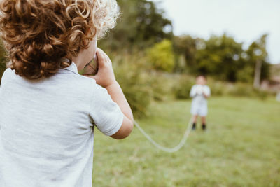 Blond boy talking through tin can phone with male friend on meadow