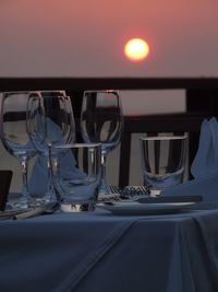 Glasses on table at restaurant against sky during sunset