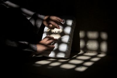 Cropped hands of person opening container with text against wall