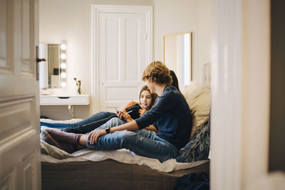 Male and female friends using technology while sitting on bed at home