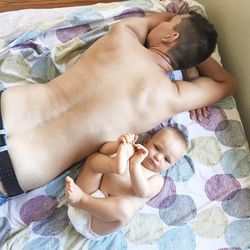 High angle view of baby boy lying by father on bed at home