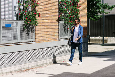 Full length of man walking on footpath by building