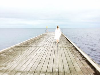 Rear view of woman on pier at sea against sky