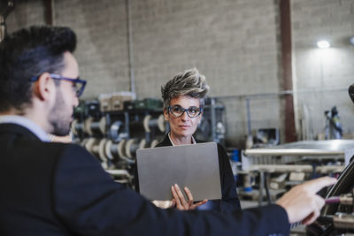 Mature businesswoman with tablet pc discussing over machinery at industry