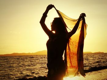 Silhouette woman standing by sea against sky during sunset