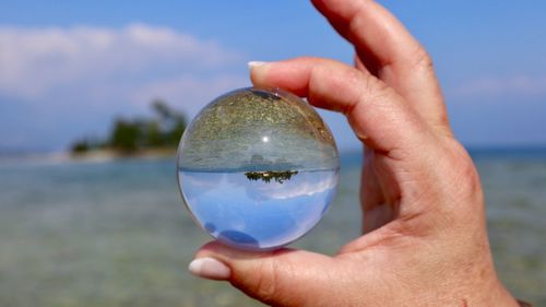 Close-up of person holding crystal ball against sky