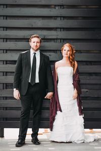 Portrait of bride and bridegroom holding hands while standing against wall