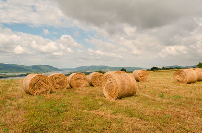 Hay bales on agricultural field against cloudy sky