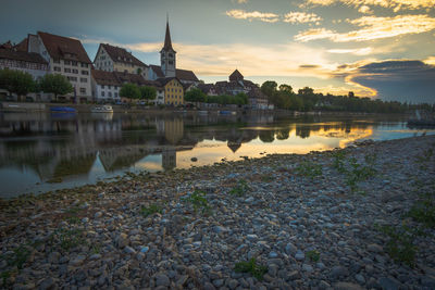 Scenic view of lake by buildings against sky during sunset