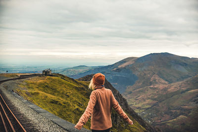 Rear view of woman looking at mountain against cloudy sky