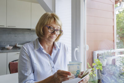 Senior woman with eyeglasses counting paper currency at home